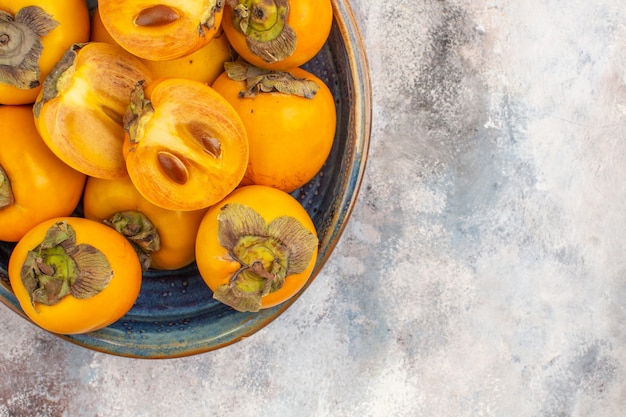 Top half view delicious persimmons in round wood box on nude background