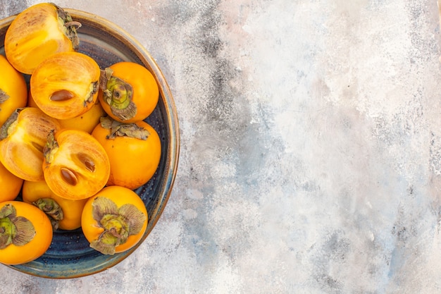 Top half view delicious persimmons in round wood box on nude background