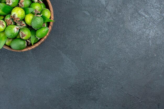 Top half view fresh feijoas in bucket on dark surface with copy space