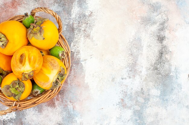 Top half view fresh persimmons in wicker basket on nude background