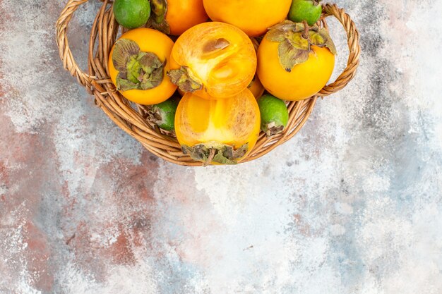 Top half view fresh persimmons in wicker basket on nude background