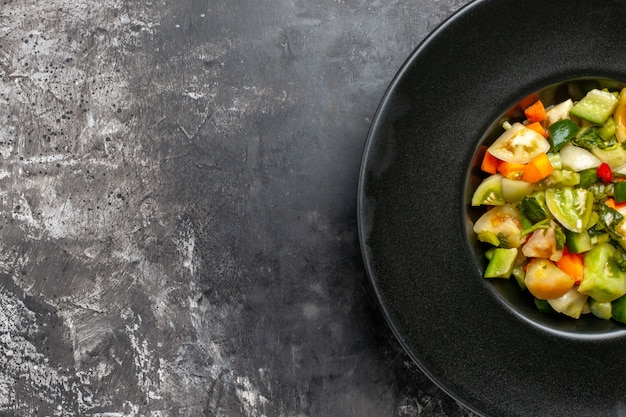 어두운 배경에 검은 타원형 접시에 상단 절반 보기 녹색 토마토 샐러드