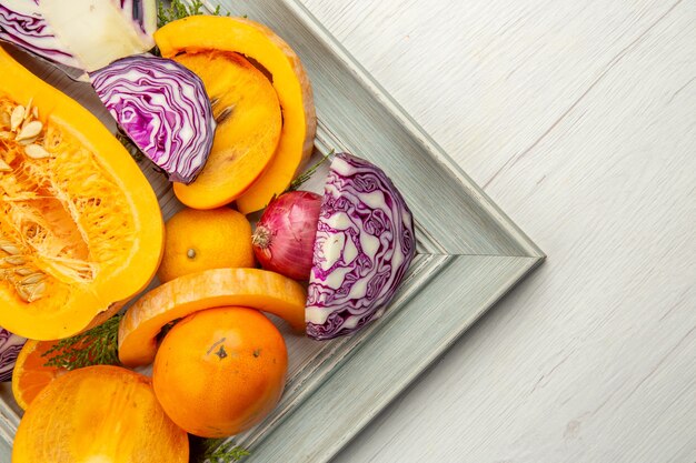 Top half view half red cabbage butternut squash persimmons red onion on frame on white wooden table