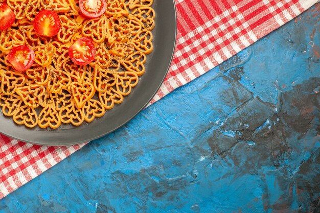 Верхняя половина зрения итальянская паста сердечки нарезанные помидоры черри на овальной тарелке на красно-белой клетчатой скатерти