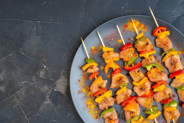 Free photo top half view raw chicken skewers with spices on wooden board on dark