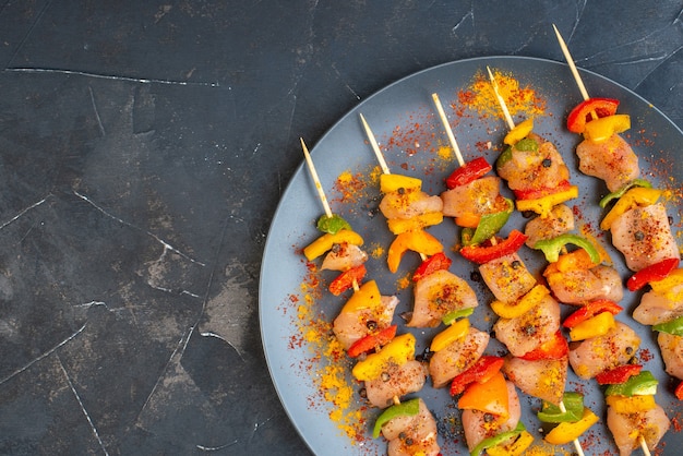 Top half view raw chicken skewers with spices on wooden board on dark