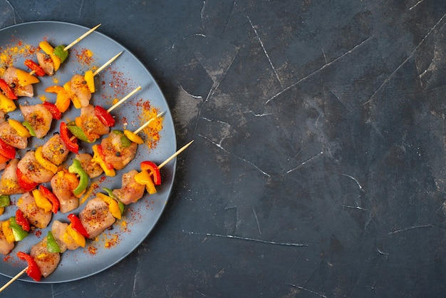 Foto gratuita spiedini di pollo crudo a metà vista dall'alto con spezie su tavola di legno su oscurità