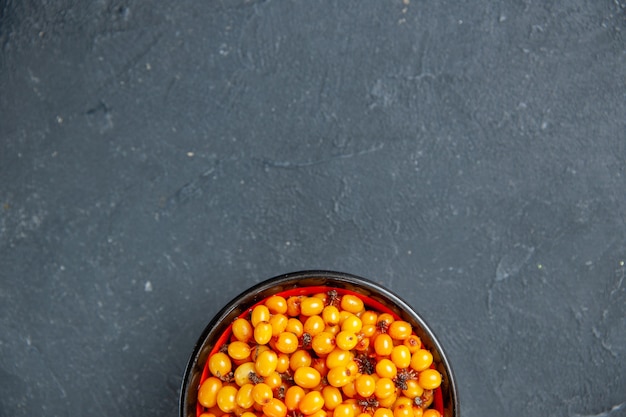 Top half view sea buckthorn in bowl on dark red surface copy space