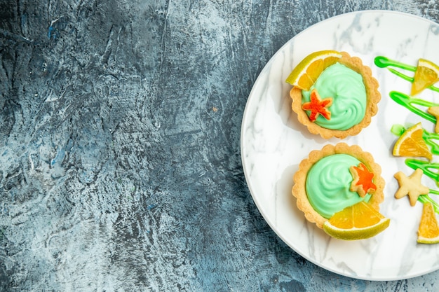 Top half view small tarts with green pastry cream and lemon slice on plate on dark surface free place