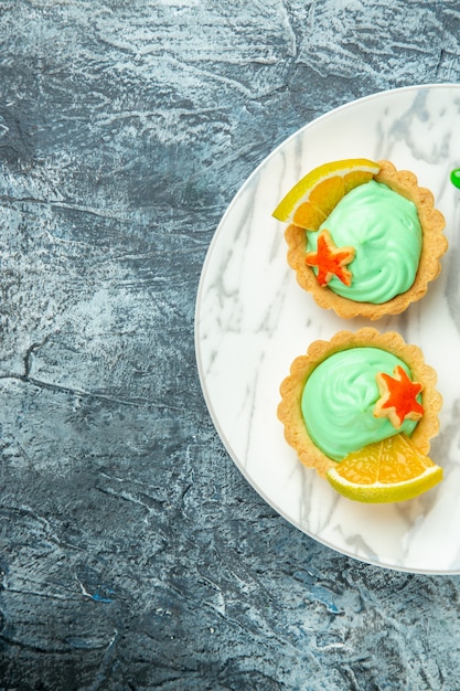 Top half view small tarts with green pastry cream and lemon slice on plate on dark surface free space