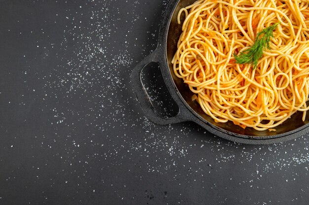 Top half view spaghetti frying pan on dark surface with free space