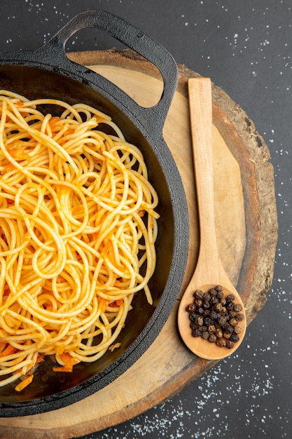 Top half view spaghetti in frying pan wooden spoon on wood board on dark surface