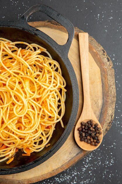 Top half view spaghetti in frying pan wooden spoon on wood board on dark surface