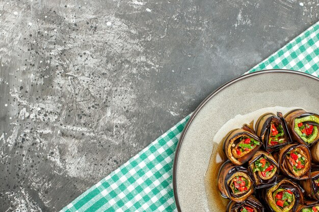 Free photo top half view stuffed aubergine rolls in white oval plate turquoise-white tablecloth on grey background