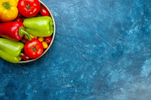Top half view vegetables cherry tomatoes different colors bell peppers tomatoes in bowl on blue table with free place