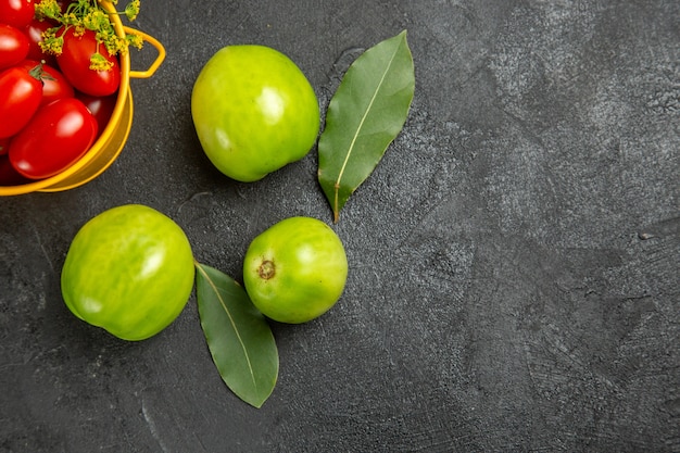 Free photo top half view yellow bucket filled with cherry tomatoes and dill flowers bay leaves and green tomatoes on dark ground