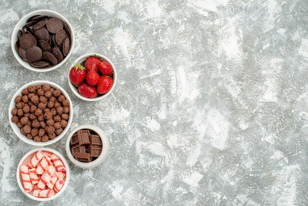 Top left side view bowls with candies strawberries bitter and milky chocolates cereals and cacao on the grey-white ground