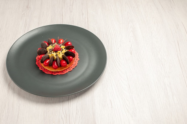 白い木製のテーブルの灰色のプレートの中央にコーネルとラズベリーで丸みを帯びた左上の側面図チョコレートケーキ