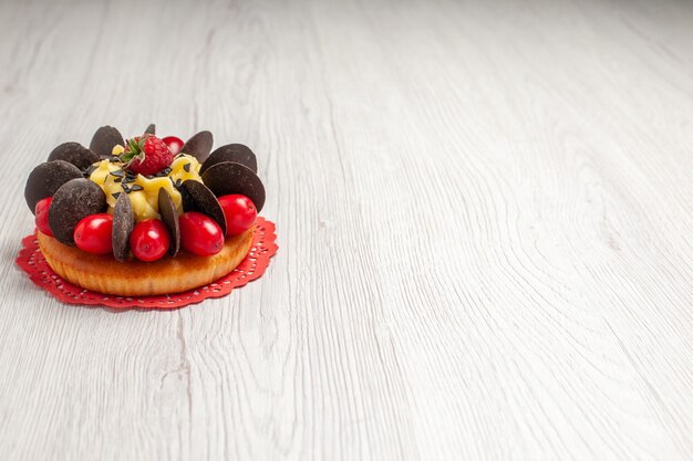 左上の白い木製のテーブルの上の赤い楕円形のレースのドイリーにベリーとチョコレートケーキを表示します。