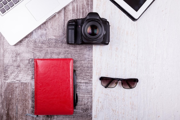 Over top photo of camera, laptop, writing notebook and sunglasses on wooden background