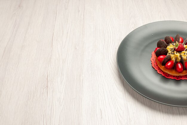 Free photo top right side view chocolate cake rounded with cornel and raspberry in the center in the grey plate on the white wooden background