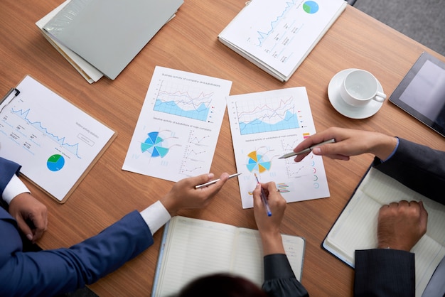 Top shot of three unrecognizable business people sitting at meeting and looking at charts