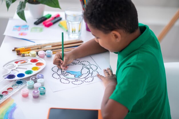 Top and side view of dark-skinned boy painting indoors