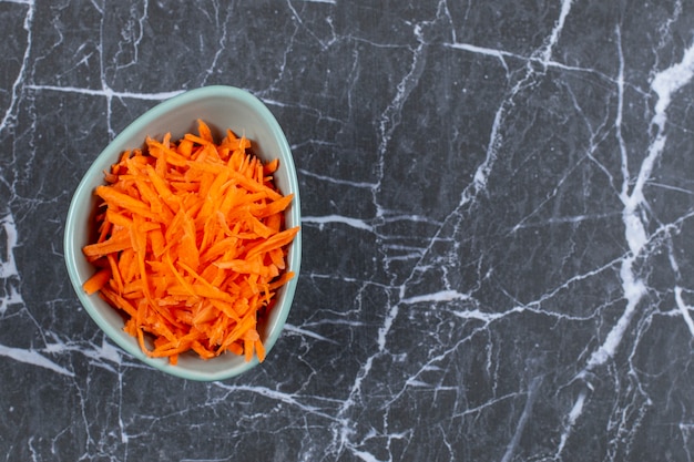 Top up view of fresh grated carrot in blue bowl over black stone.