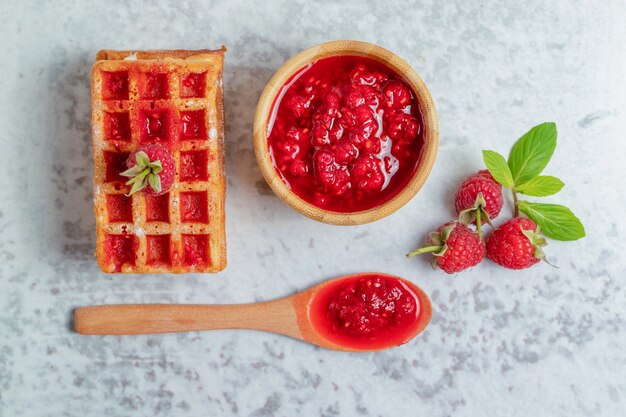 Top up view of fresh waffle with raspberry jam. 