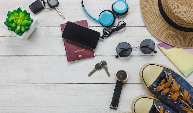 Free photo top view accessoires to travel concept. mobile  phone listening music by headphone on wooden background.shoes,passport,watch,sunglasses and hat on wood table.