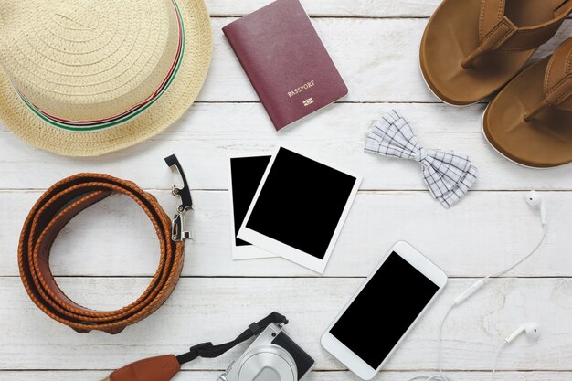 상위 뷰 accessoires 여행 개념. 흰색 휴대 전화, 모자, 여권, 카메라, 사진, 나무 테이블에 샌들.