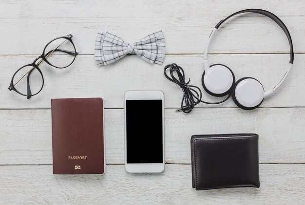 Top view accessoires to travel with man clothing concept. bow tie,passport on wooden background.eyeglasses,headphone,wallet,tree on wood table.