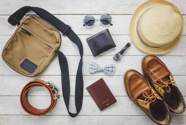トップビューaccessoires男性服のコンセプトで旅行する。蝶ネクタイ、木製の背景にウォレット。ウォッチ、サングラス、バッグ、帽子、ベルト、木製テーブル上の靴。