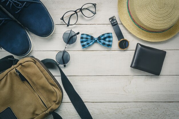 Top view accessoires to travel with man clothing concept. bow tie,wallet on wooden background.watch,sunglasses,bag,hat and shoes on wood table.
