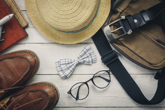 トップビューaccessoires男性服のコンセプトで旅行する。弓、木製のbackground.watch、眼鏡、バッグ、帽子、飛行機、白い木製のテーブル上のマップ。