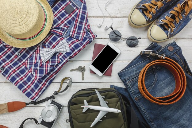 Вид сверху, чтобы путешествовать с концепцией мужской одежды. рубашка, джинс, мобильный телефон, наушники на деревянный background.passport, ключ, солнцезащитные очки и шляпа на деревянный стол.
