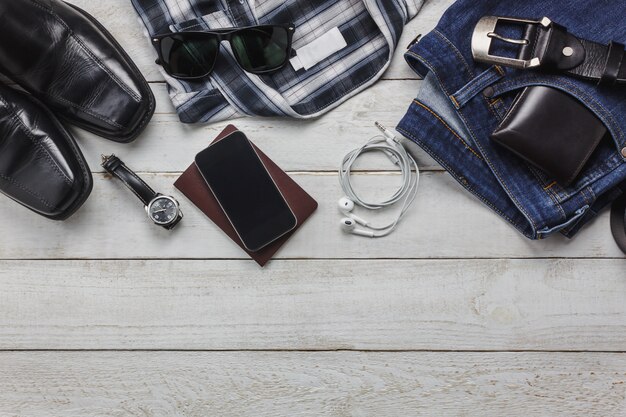 Top view accessoires to travel with man clothing concept. shirt,jean,mobile phone on wooden background.watch,sunglasses and shoes on wood table.