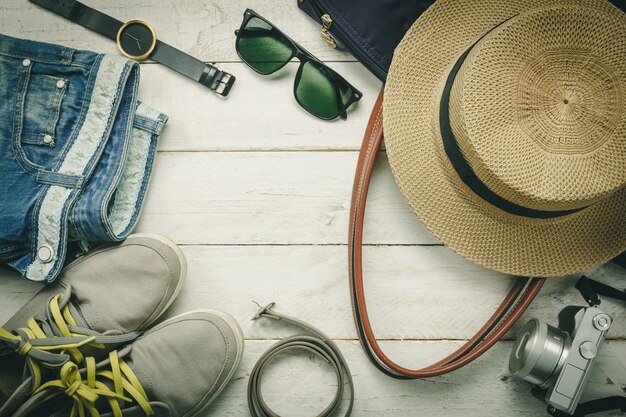 Top view accessoires to travel with women clothing concept.belt,bag,hat,camera,necklace,trousers,watch and sunglasses on white wood table background.flat lay,fashion woman.copy space.