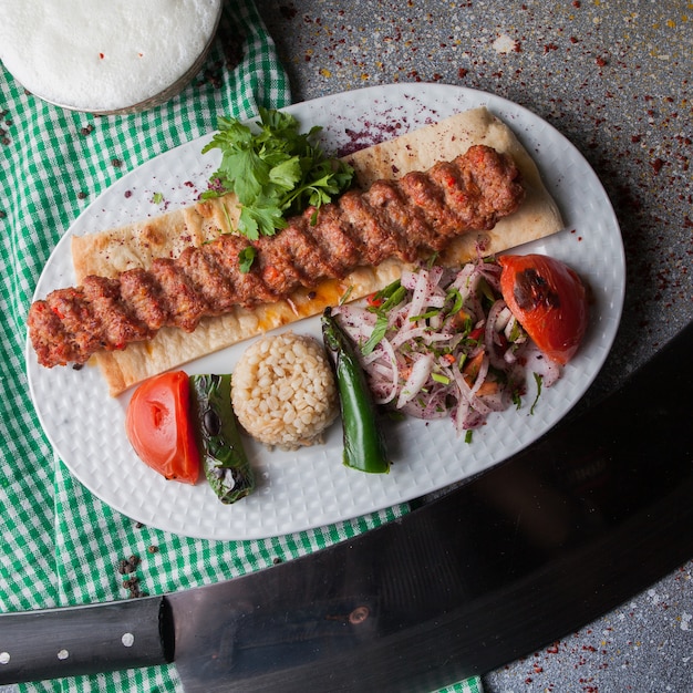 Top view adana kebab with rice and fried vegetables and chopped onion and ayran in white plate