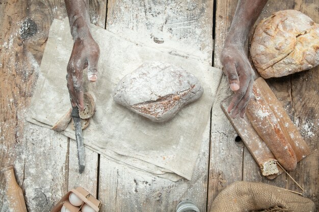 Вид сверху афроамериканца готовит свежие хлопья, хлеб, отруби на деревянном столе