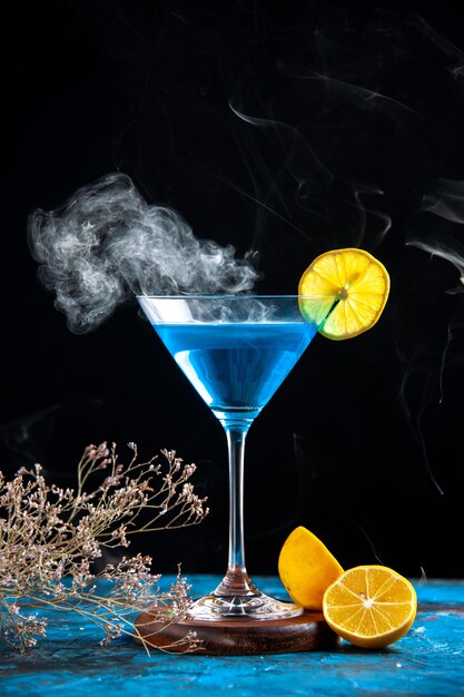 Top view of alchocol cocktail in a glass goblet served with lemon slice and fir branches on blue table