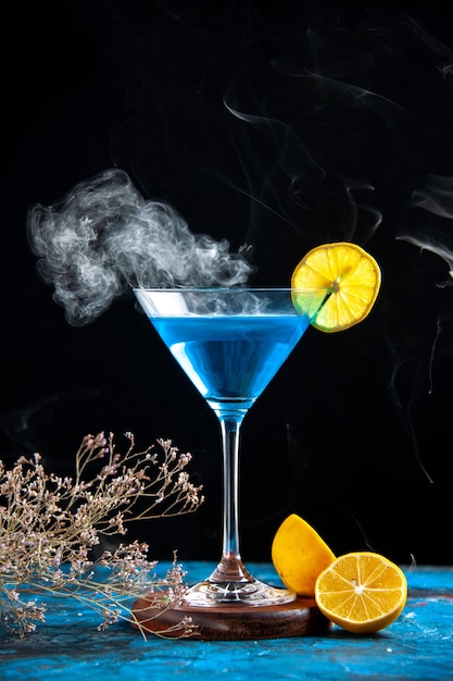 Top view of alchocol cocktail in a glass goblet served with lemon slice and fir branches on blue table