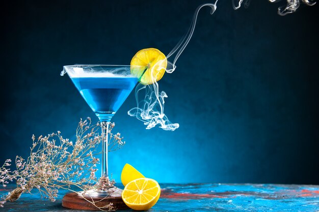 Top view of alchocol cocktail in a glass goblet served with lemon slice and fir branches on the right side on blue table