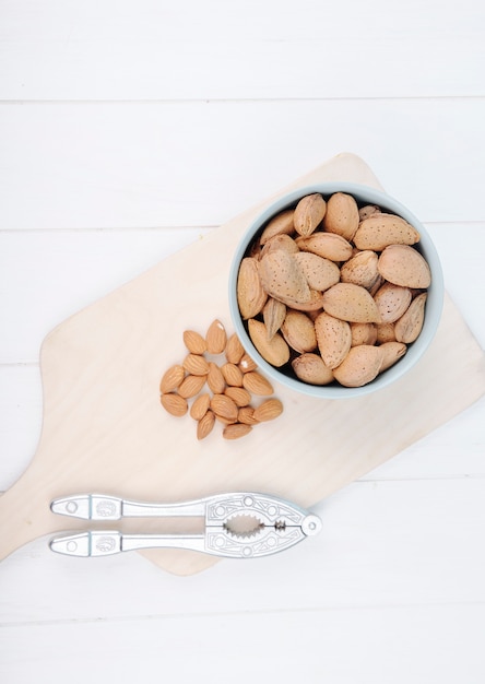 Top view of almond in a bowl with nut cracker on wooden board on white background with copy space