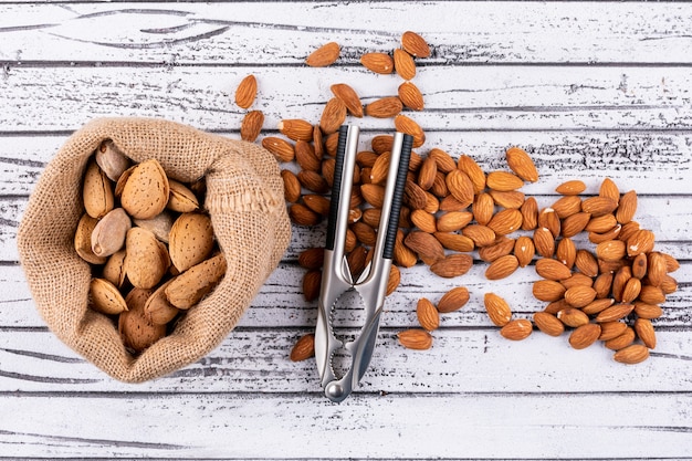 Top view almond and a sack of almond with nut cracker on white wooden table. horizontal