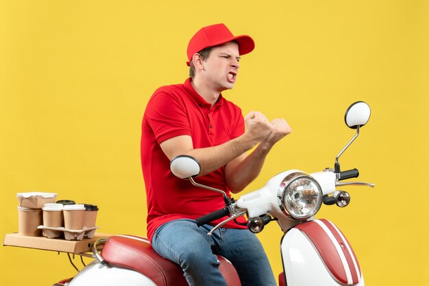 黄色の背景に注文を配信赤いブラウスと帽子を身に着けている野心的な感情的な若い男の上面図