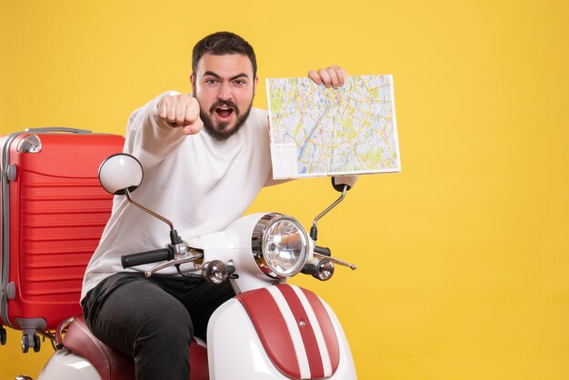 Top view of ambitious young guy sitting on motorcycle with suitcase on it holding map on isolated yellow background