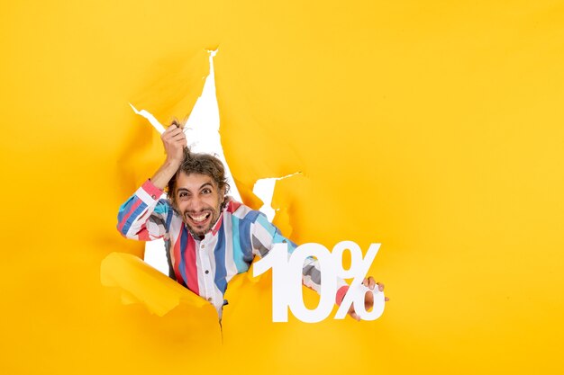 Top view of angry young man showing ten percentage in a torn hole in yellow paper