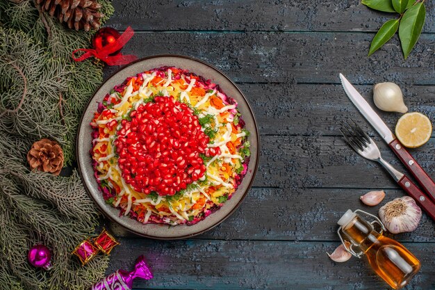 Вид сверху аппетитное блюдо Рождественское блюдо с зернами граната рядом с бутылкой масла вилка нож ветки дерева лимон и чеснок