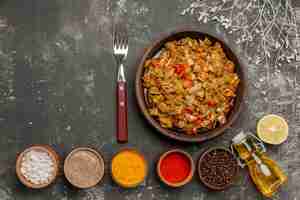 Free photo top view appetizing food brown plate of green beans and tomatoes next to the spices in bowls fork lemon and bottle of oil on the black table